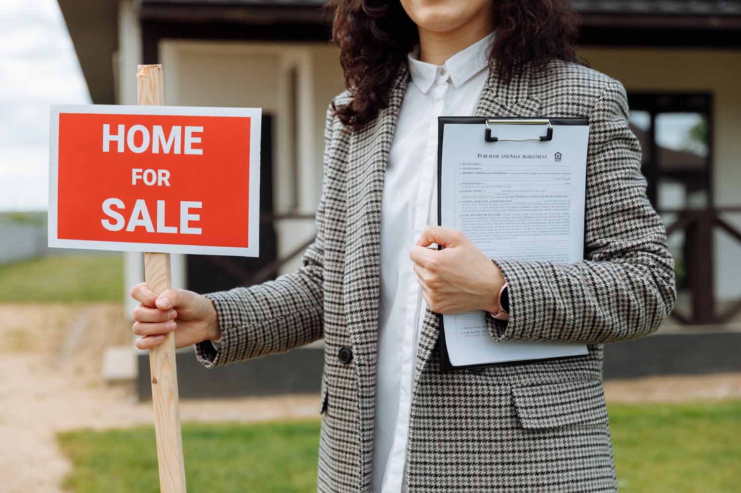 Woman in front of a house holding a Home for Sale sign and a clipboard