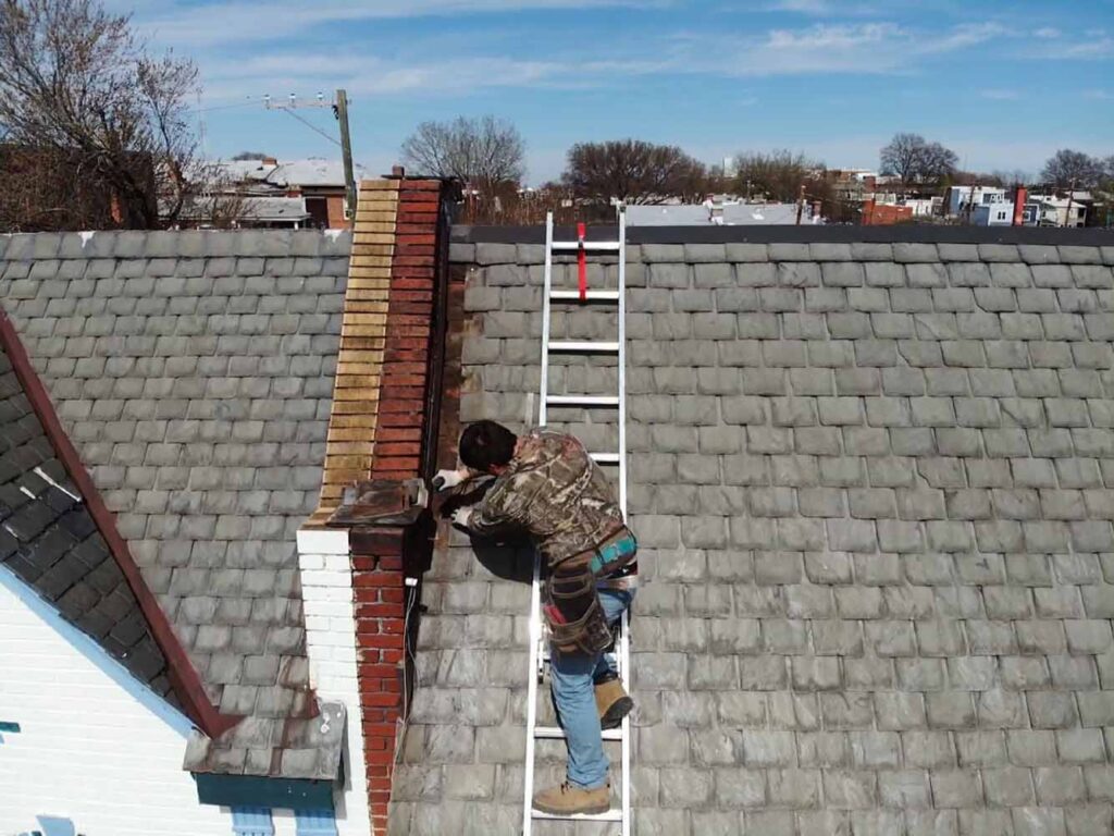 Man on ladder making repairs to a slate roof