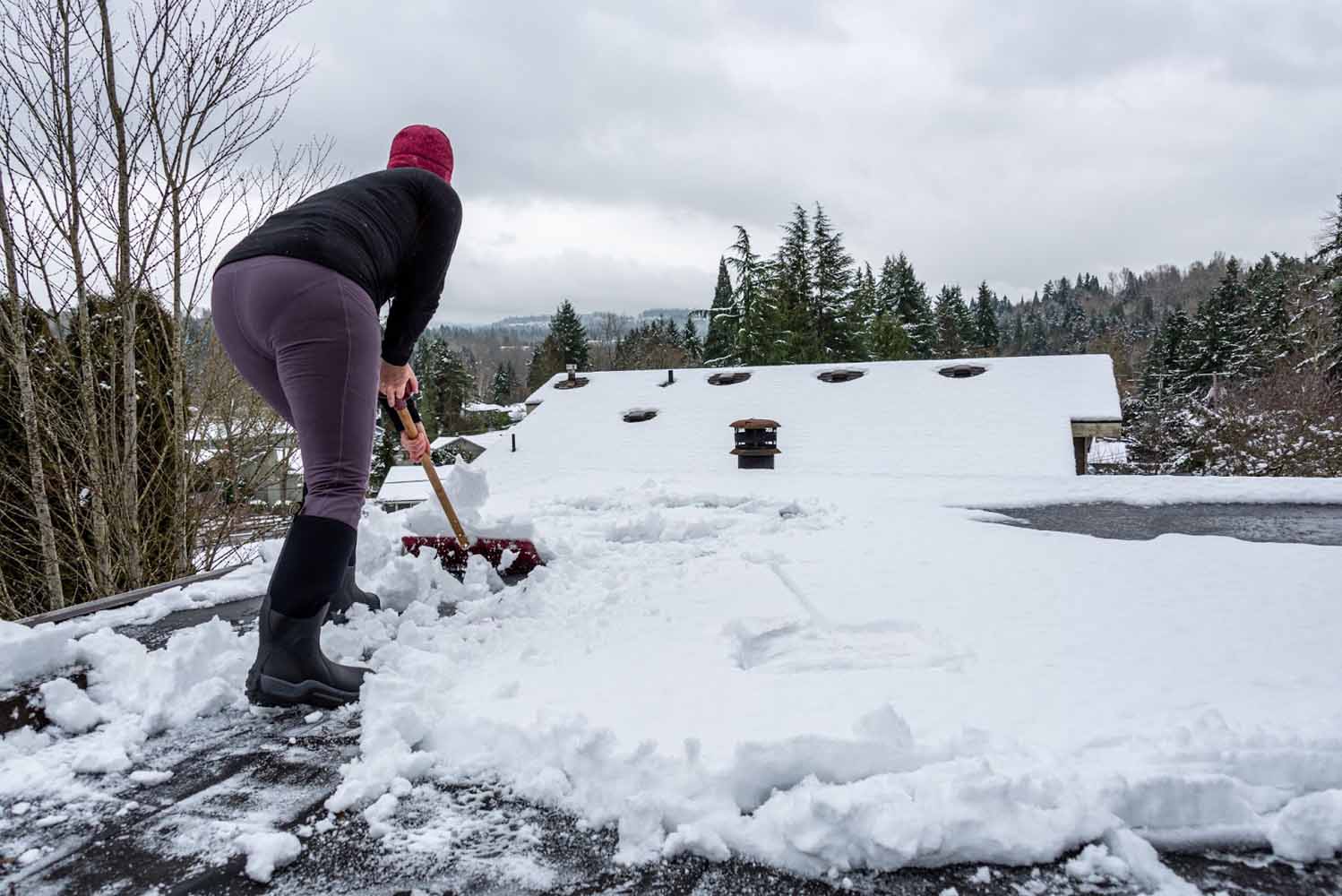 Woman shoveling snow off a flat portion of her roof