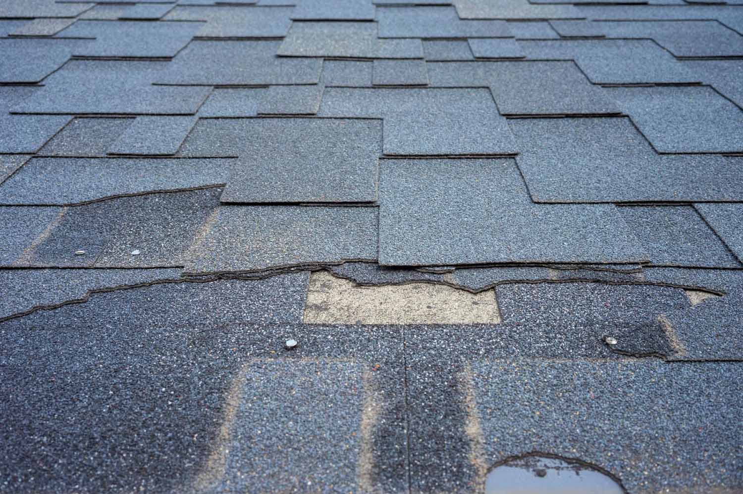 Close up image of a shingle roof that has missing and torn shingles, cause by wind damage.