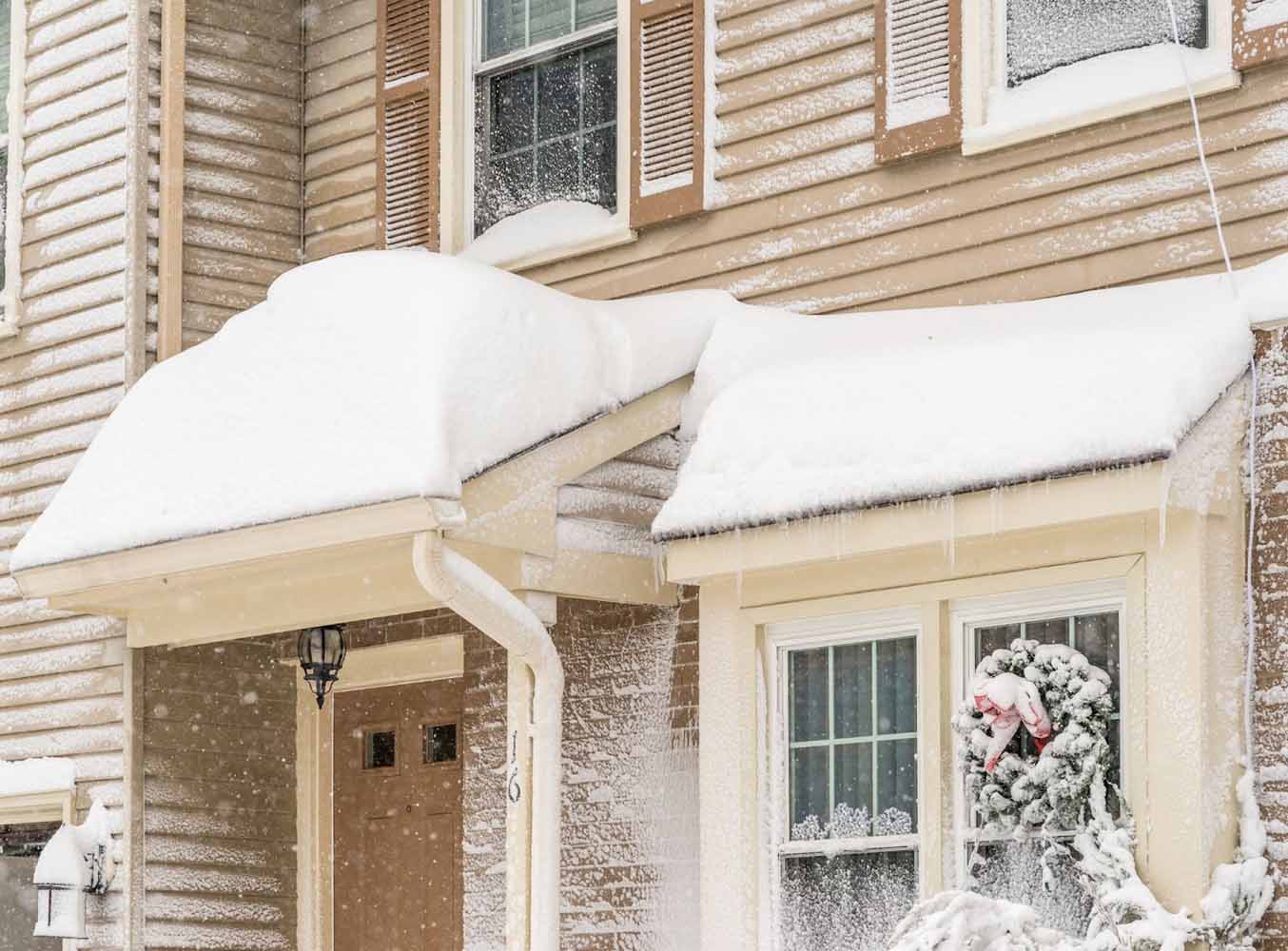 A large amount of snow on the roof of a tan home during a snowstorm