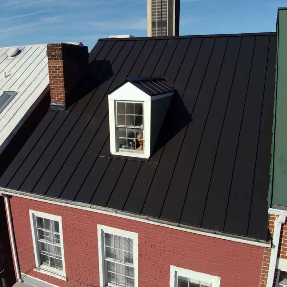 Red brick building with a black metal roof and a small dormer window. 