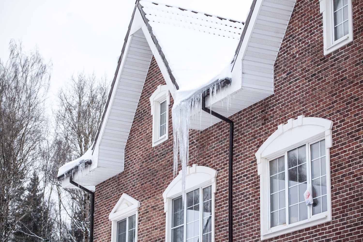 Red brick home in the winter with a buildup of snow and ice on the roof