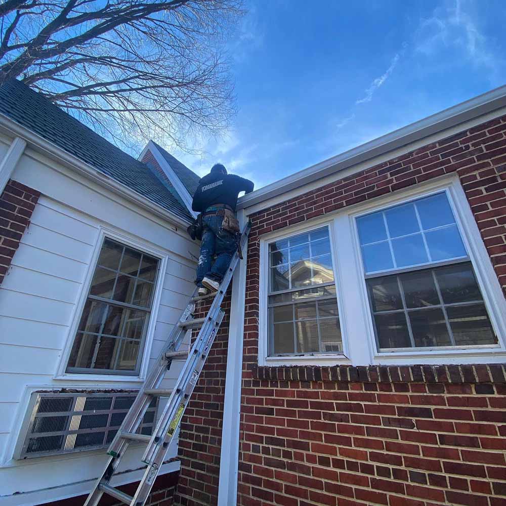 Hammersmith roofing professional on a ladder, cleaning the gutters and inspecting the roof for a client