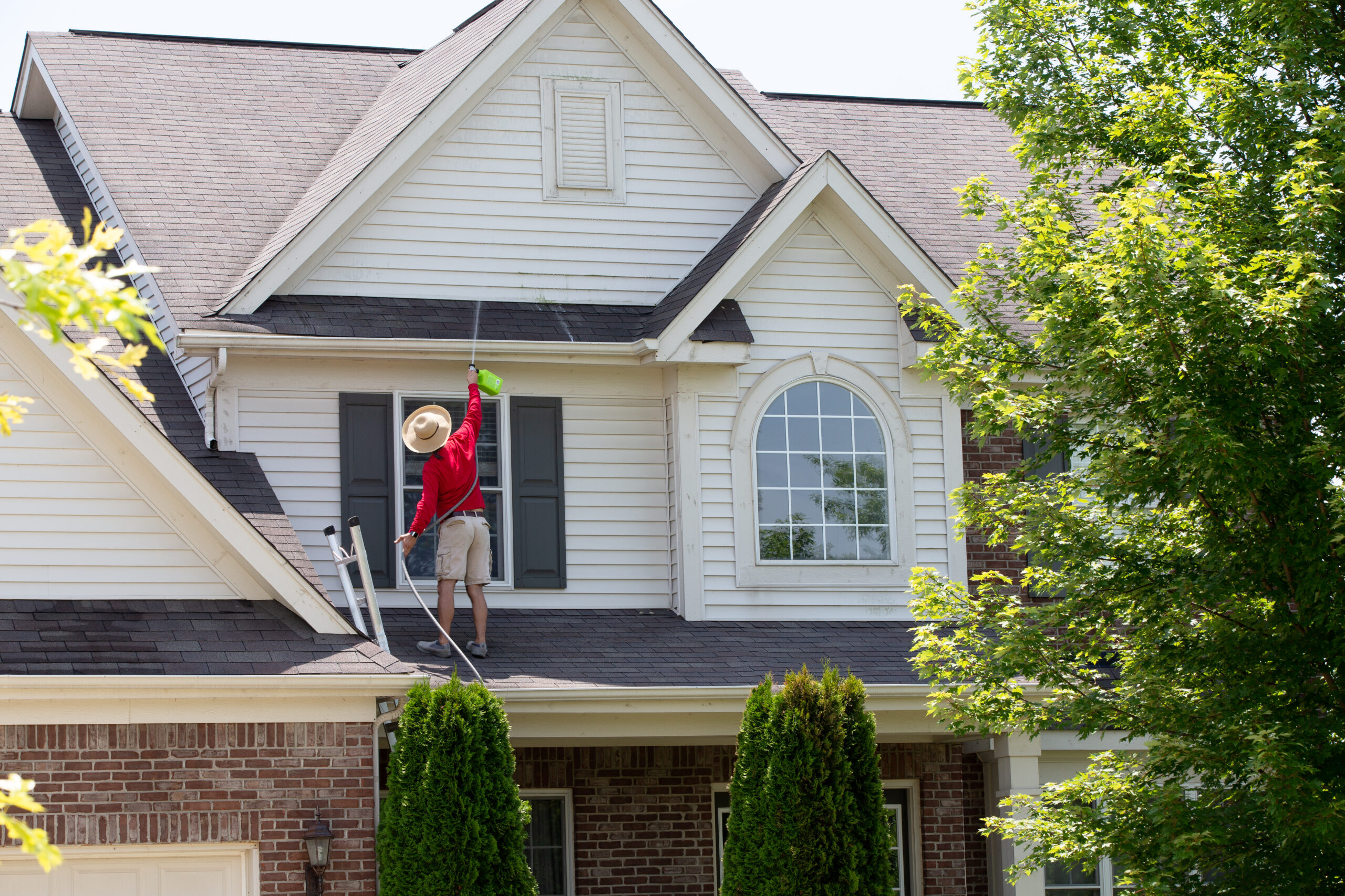 Homeowner cleaning the roof of his home using a cleaning solution attached to a garden hose