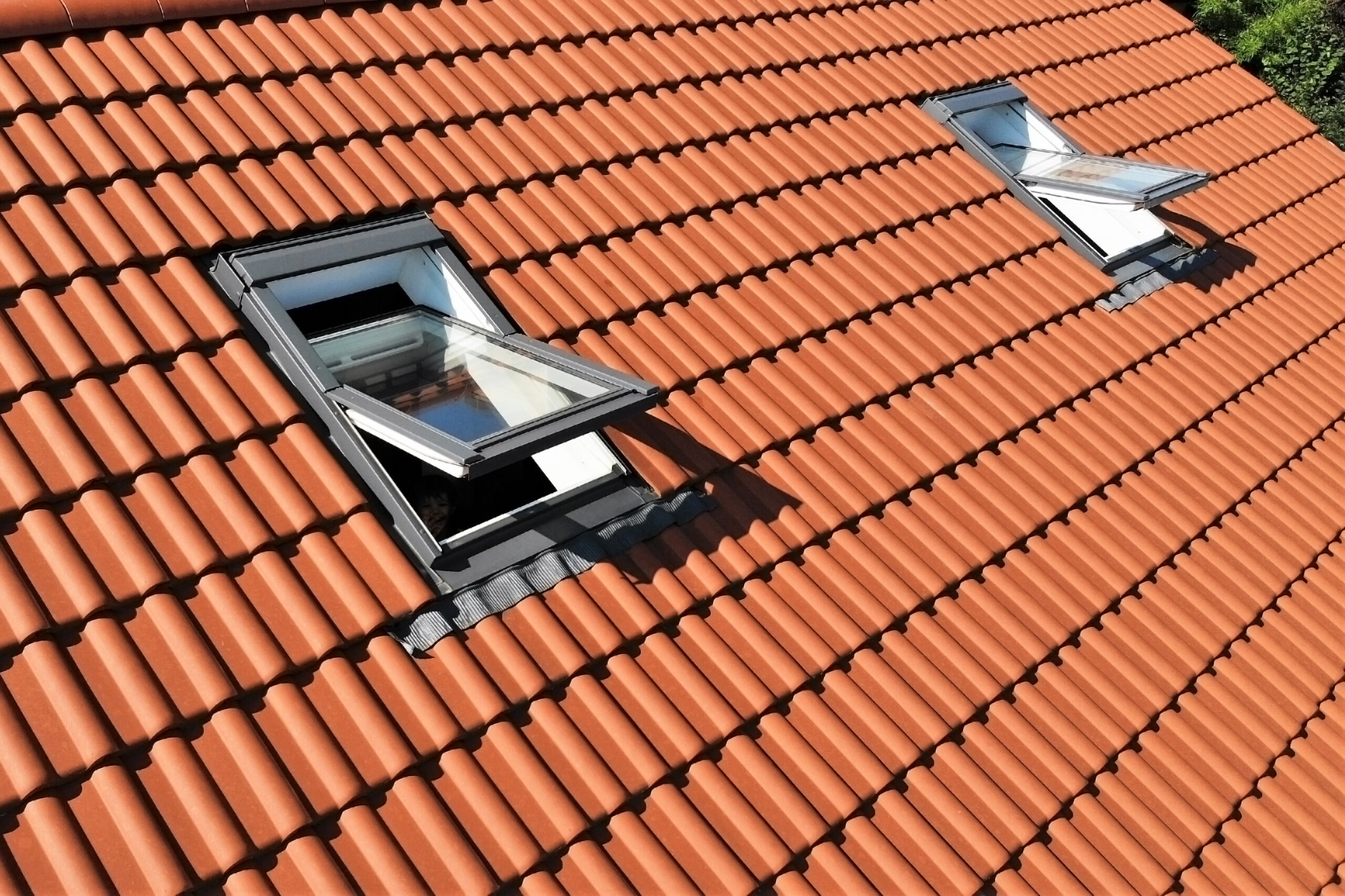 Two ventilated skylights, both in the open position, on a clay tile roof 