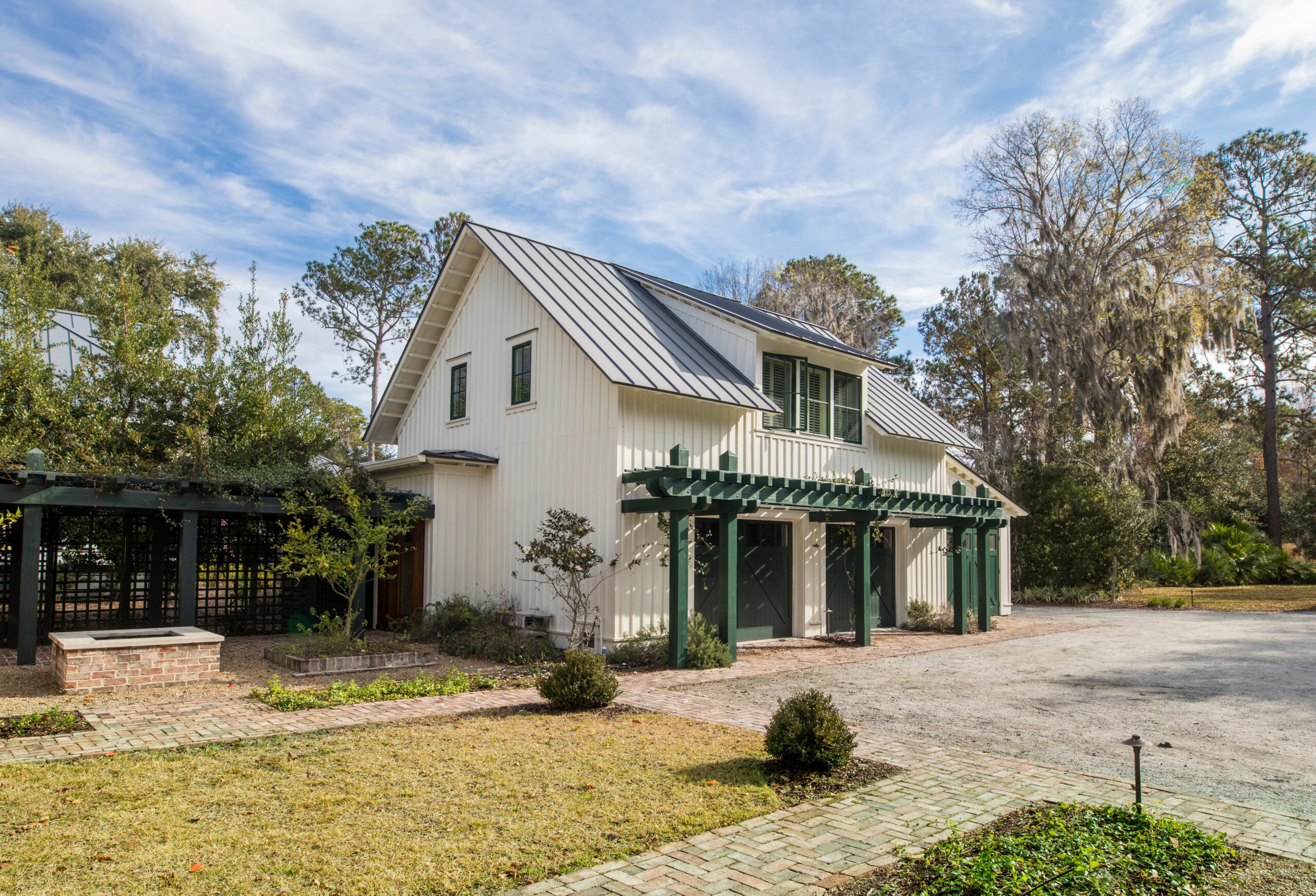 Off-white detached garage with a black metal roof and green awning trellis