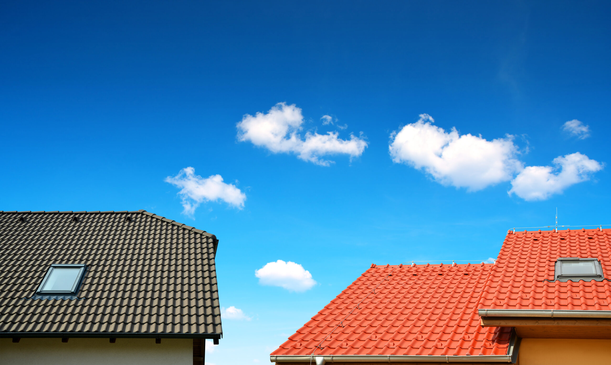 House with a dark brown roof on the left and a house with a red roof on the right, on a blue sky background