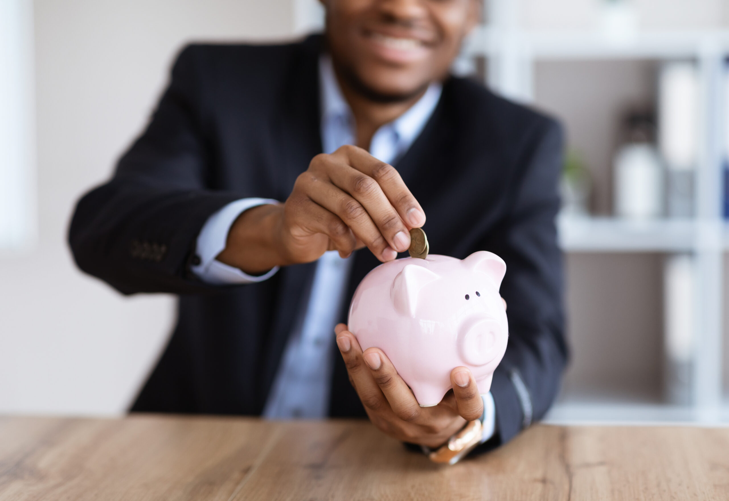 Man in business suit puts money into a piggy bank after saving money by investing in regular roof maintenance