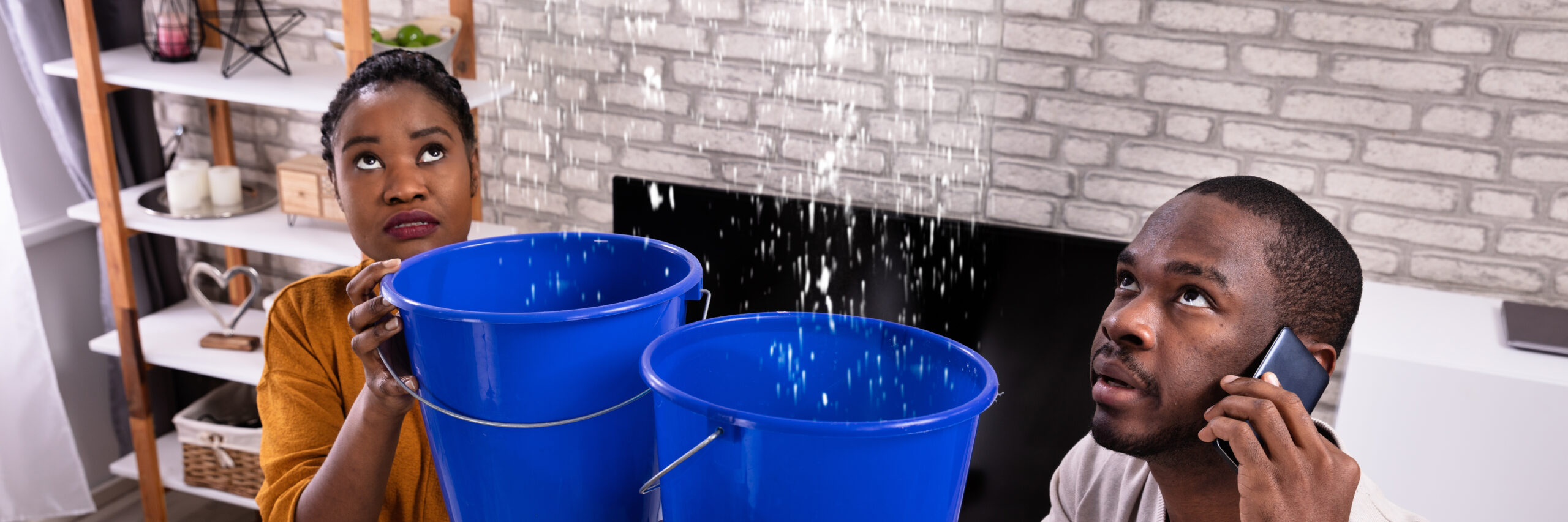 Couple holding buckets and staring at water leaking from ceiling