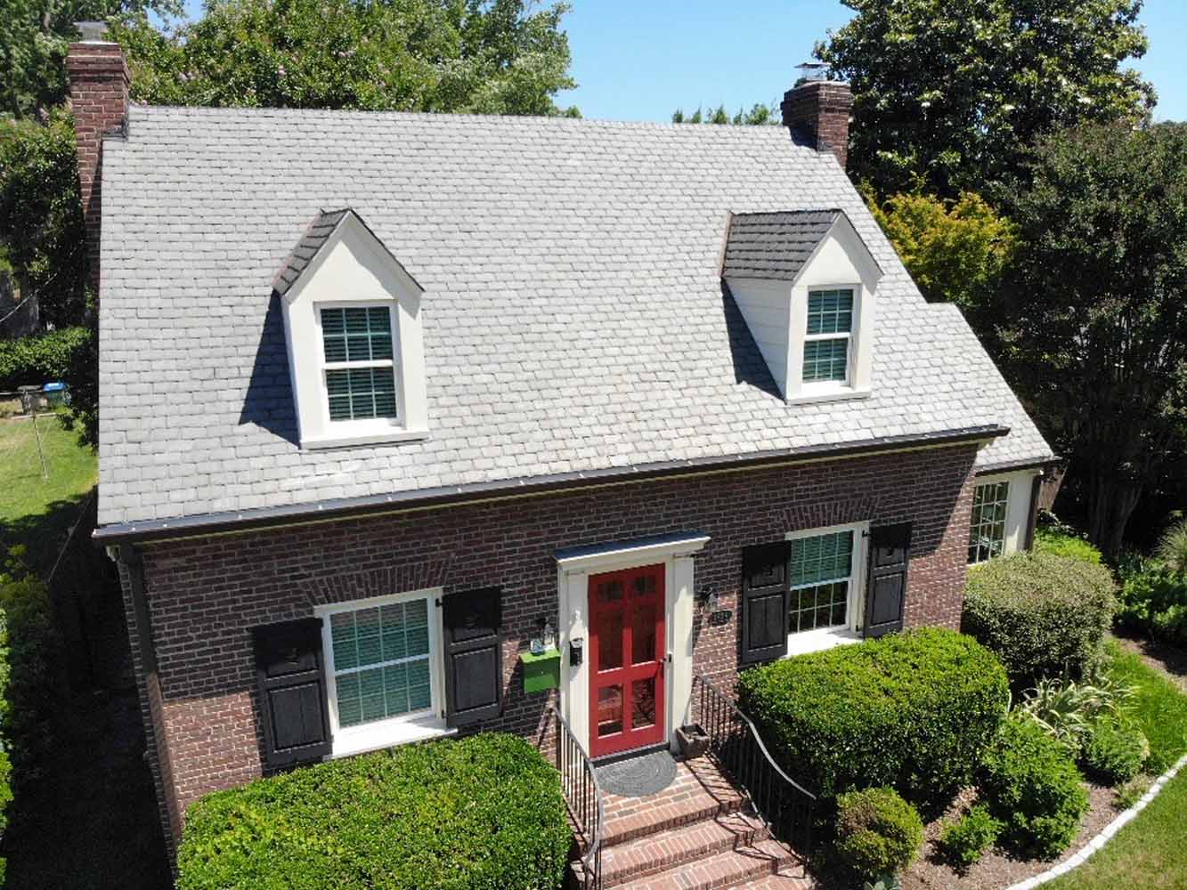 Aerial view of a residential brick house with a newly installed gray shingle roof by Hammersmith Roofing. 
