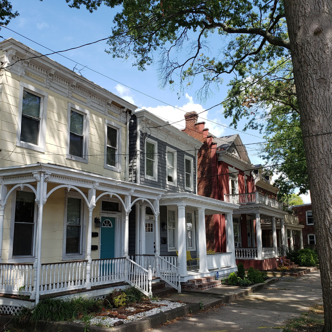 Historic row houses with ornate porches and a tree-lined sidewalk on a sunny day 