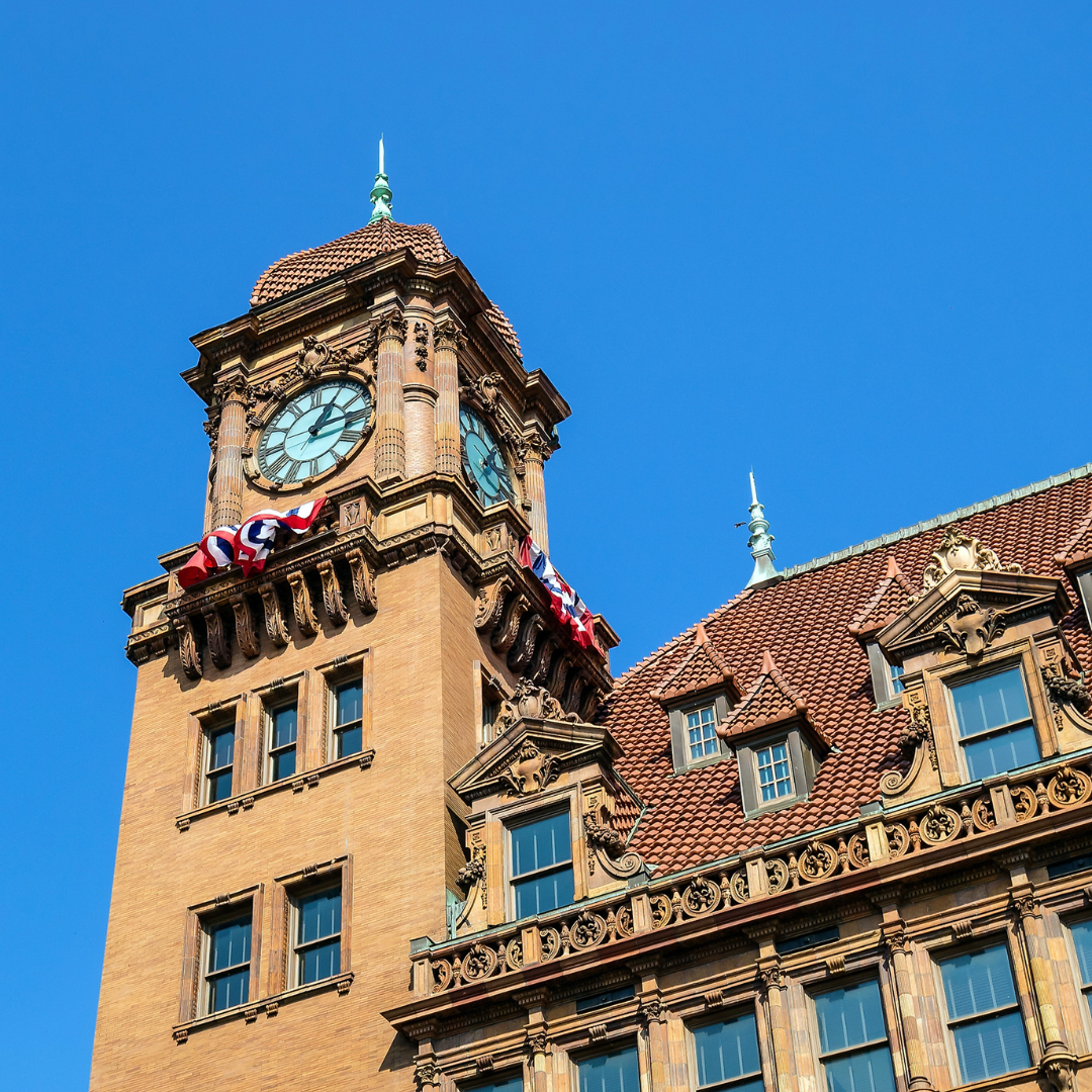 Historic building tower with a clock and draped American flags under a clear blue sky 