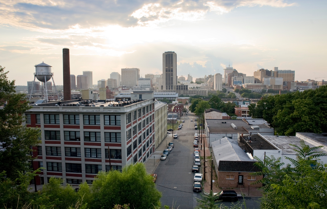 Sunrise over an urban landscape with a water tower, smokestack, and modern city skyline in the background. 