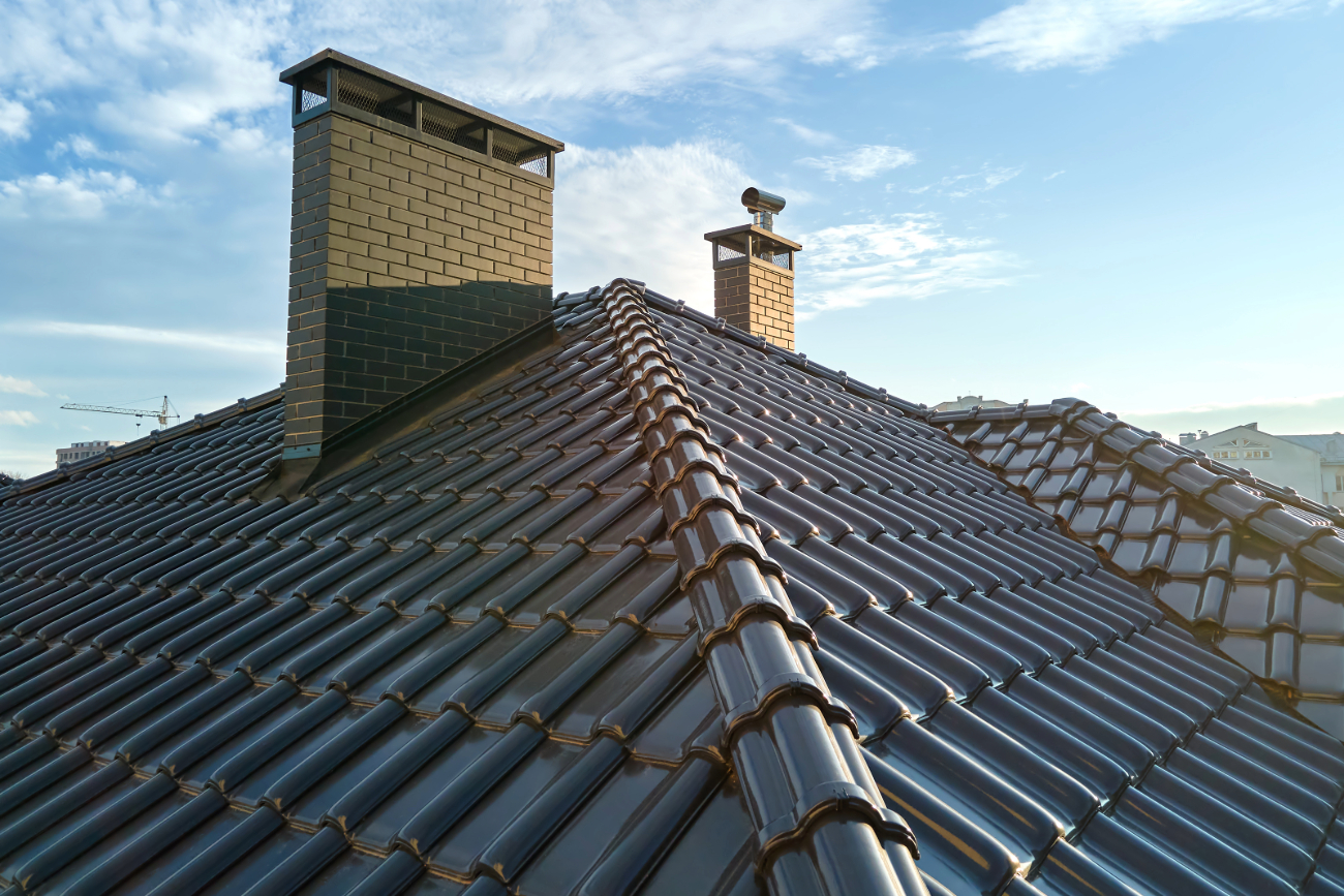 Close-up of a tiled roof with two brick chimneys against a cloudy sky. 