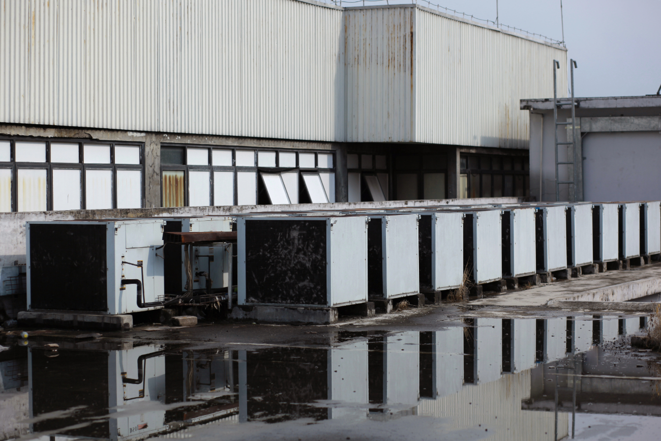 Reflection of a dilapidated industrial building with rusty walls and a row of vents in a puddle. 