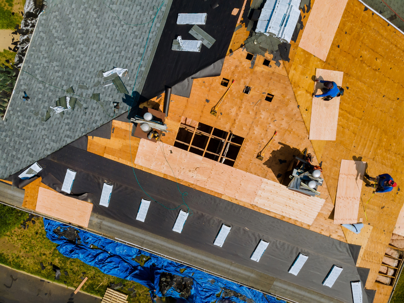 Aerial view of workers installing a new roof with sections of plywood and roofing materials visible. 