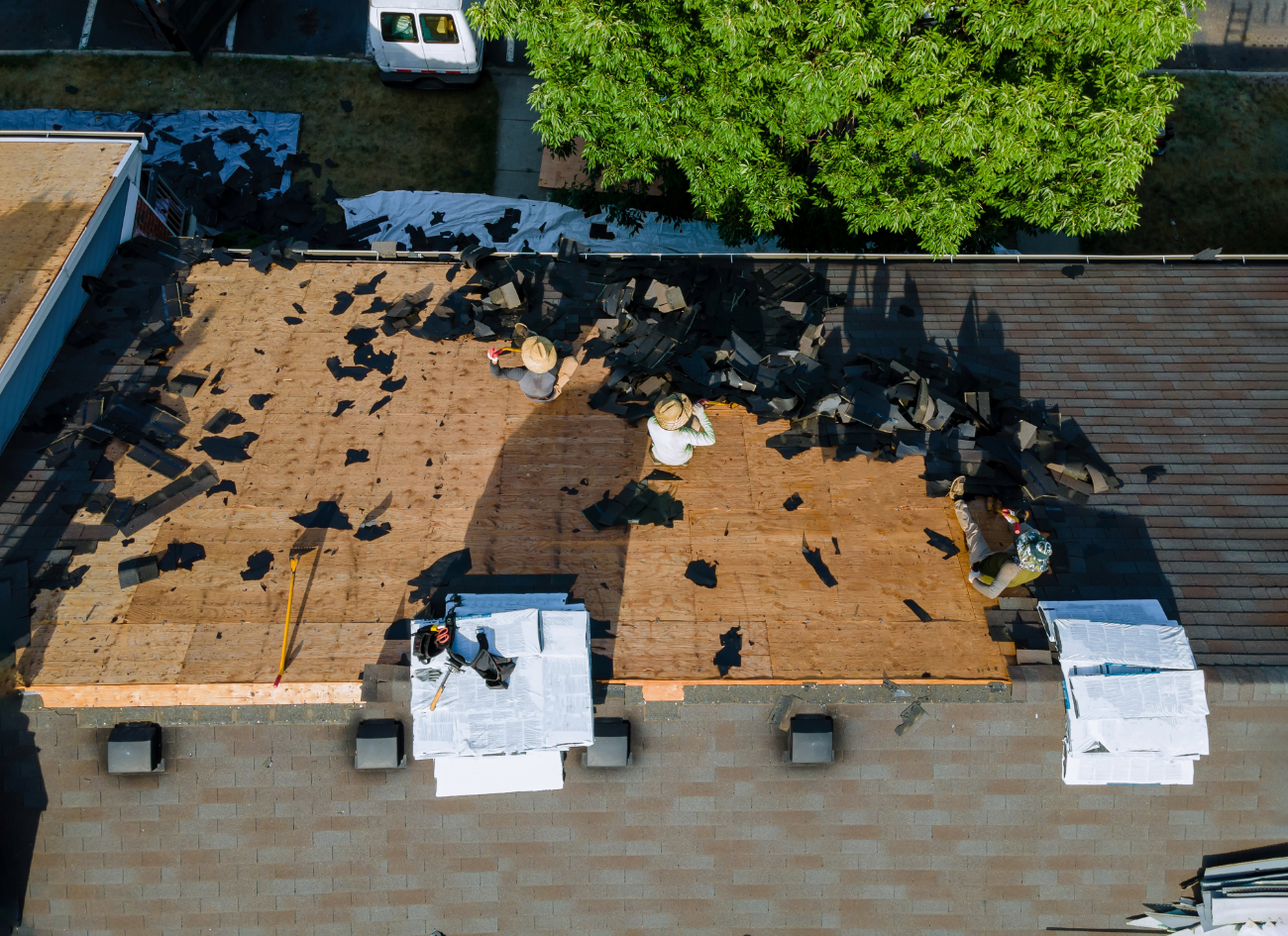 Aerial view of workers removing old shingles during a roof renovation, with scattered debris and tools. 