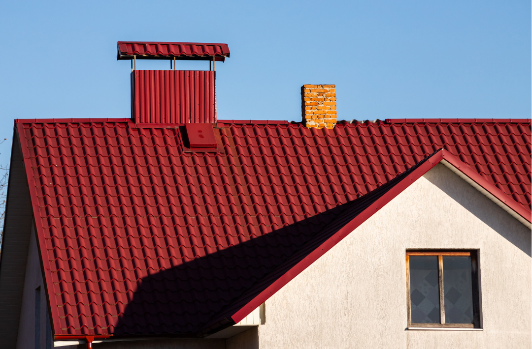 Red metal roof with a decorative chimney and a rooftop vent on a house. 