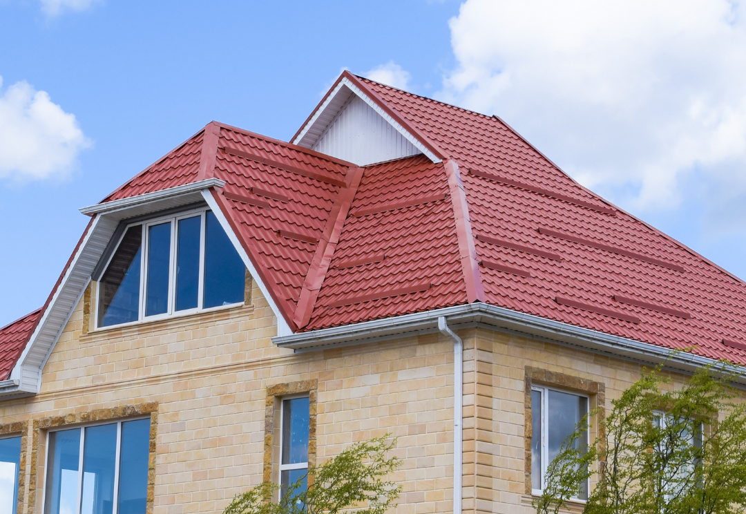 Red tiled roof on a cream-colored stone house with multiple gables and windows. 