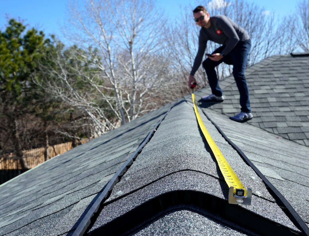 Man measuring the roof ridge with a tape measure, focusing on precision in a residential setting. 