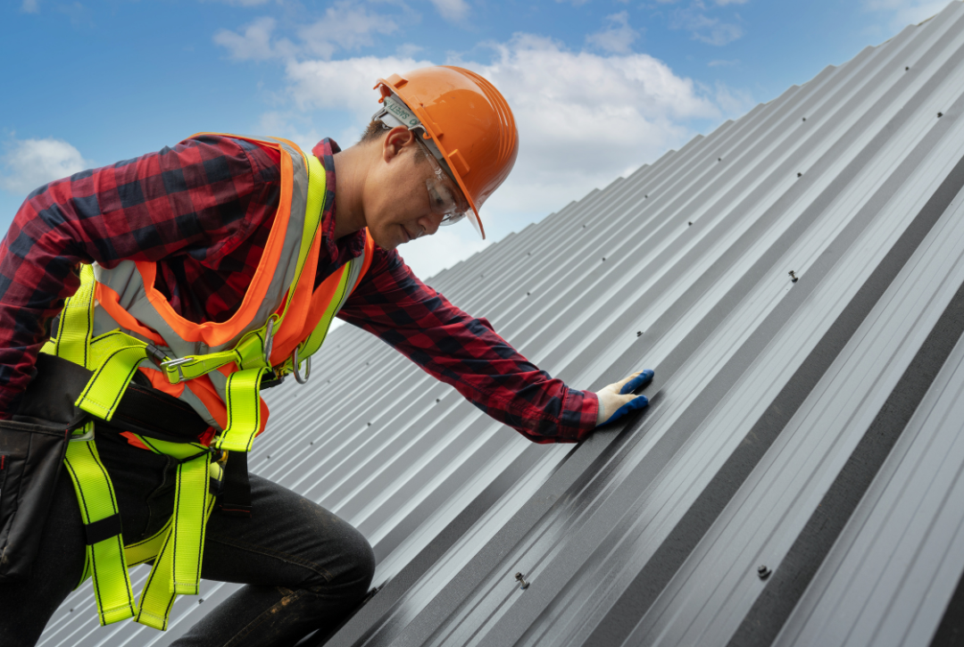 Construction worker in safety gear inspecting a metal roof. 