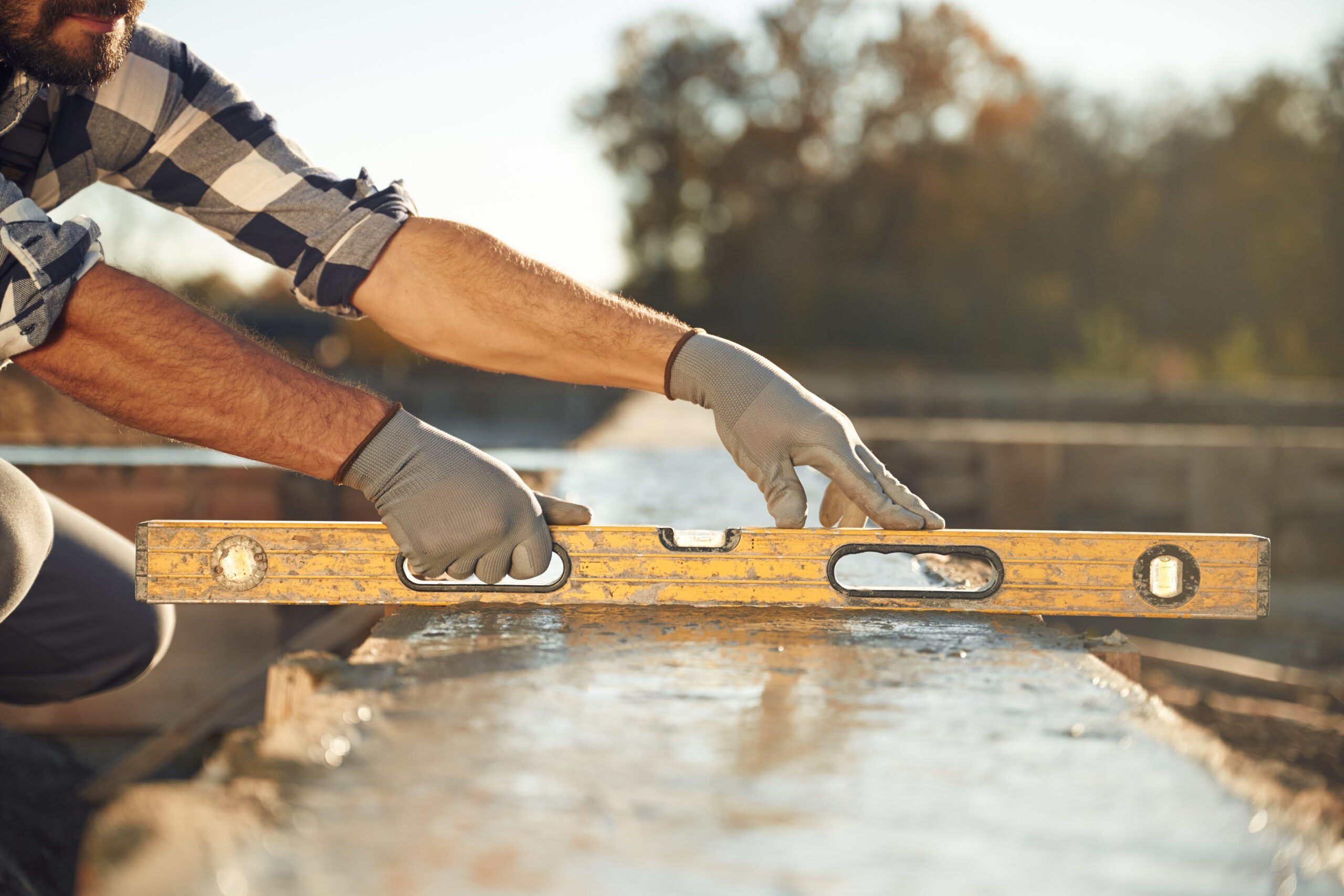 Worker wearing gloves carefully aligning a level tool on a construction site, showcasing craftsmanship for roofers near me.