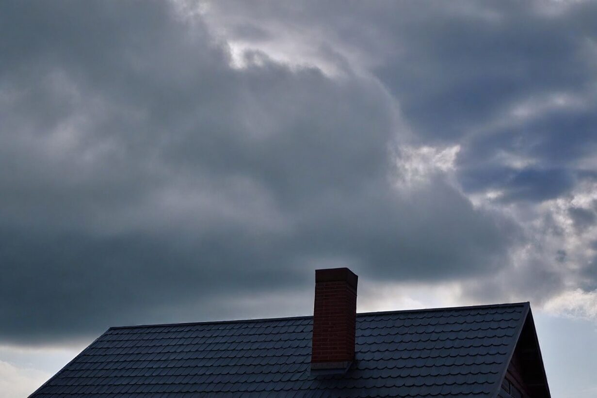 A house against a dark and stormy background, that may need roofing contractors to do repairs after the storm.